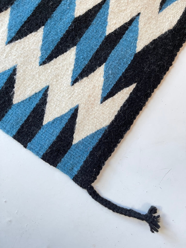 Close-up of a geometric-patterned rug with blue and black triangles on a white background