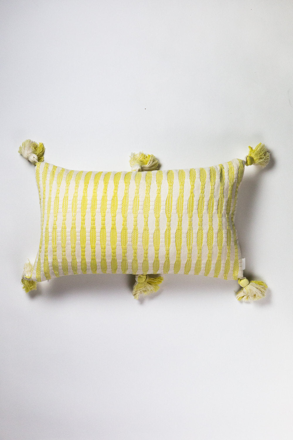 Yellow and white striped pillow with tassels on a light gray background