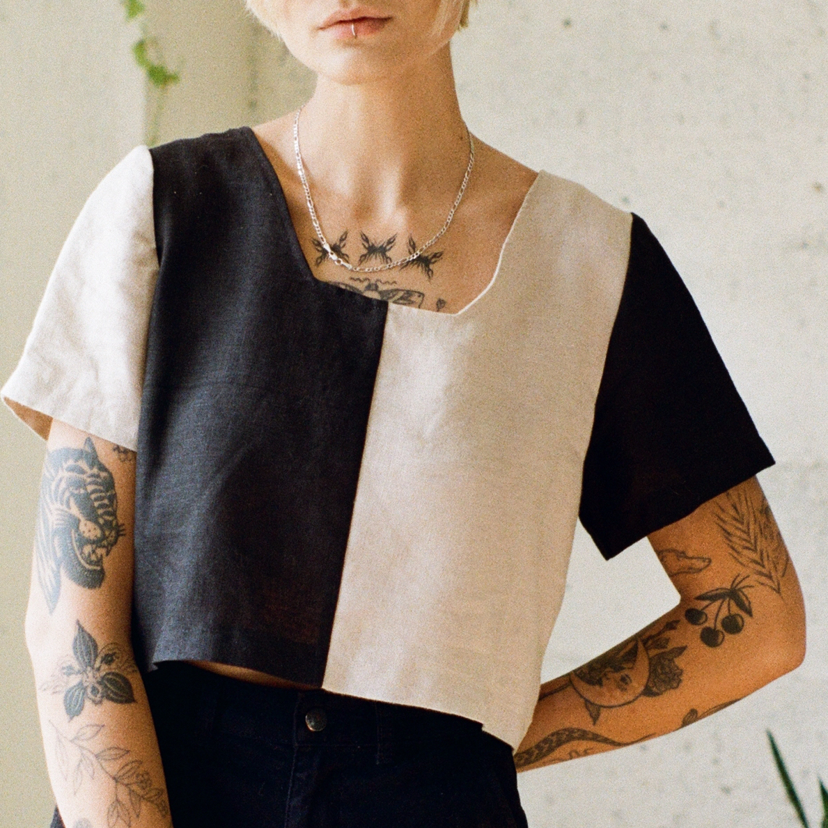 Person wearing a black and beige geometric top with tattoos on arms and neck.