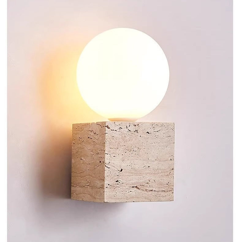 Wall-mounted light fixture with a stone base and round glass cover on a neutral background
