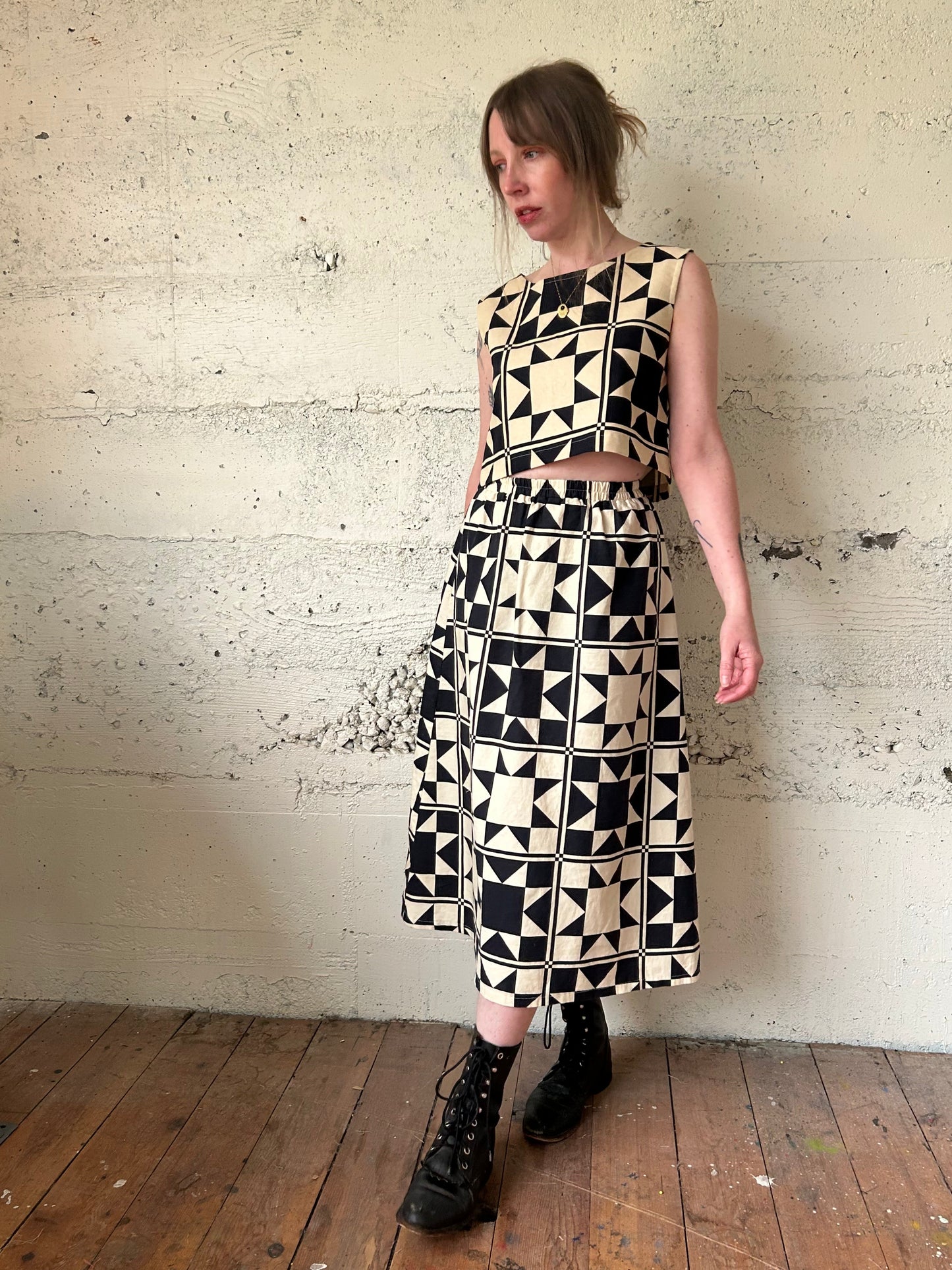 Woman wearing a black and white geometric patterned dress against a textured wall.