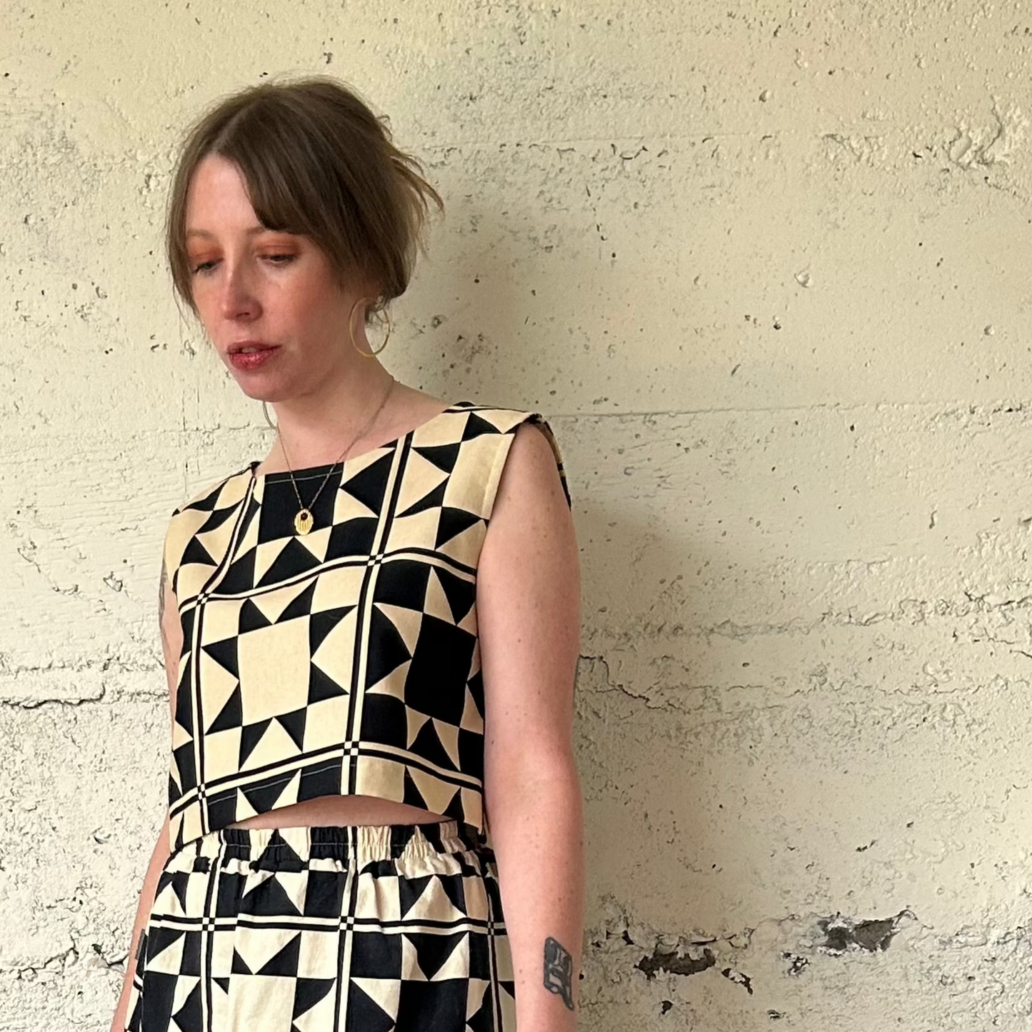 Woman wearing a black and white geometric dress against a textured beige wall.