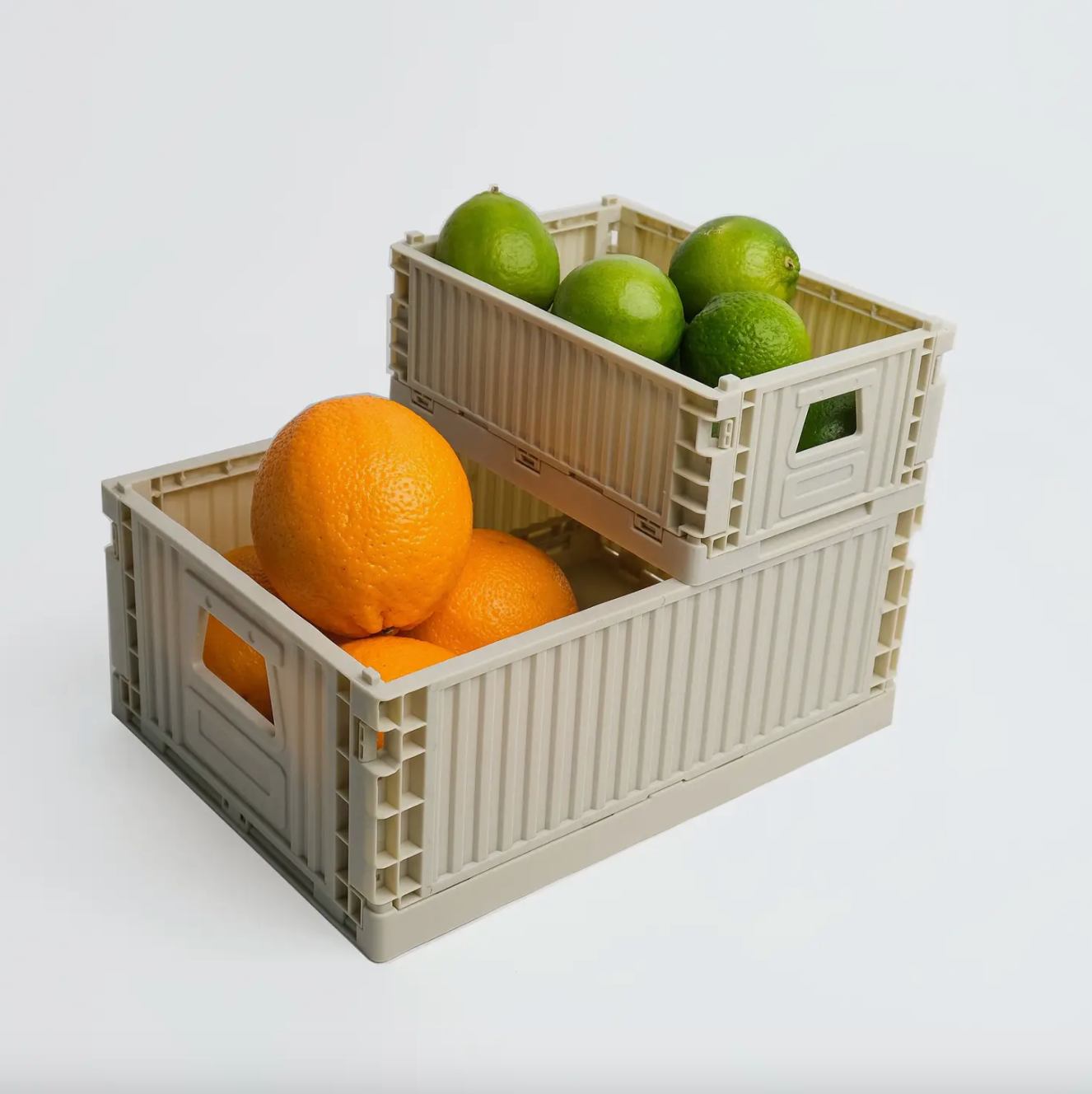 Two beige crates with oranges and limes on a white background