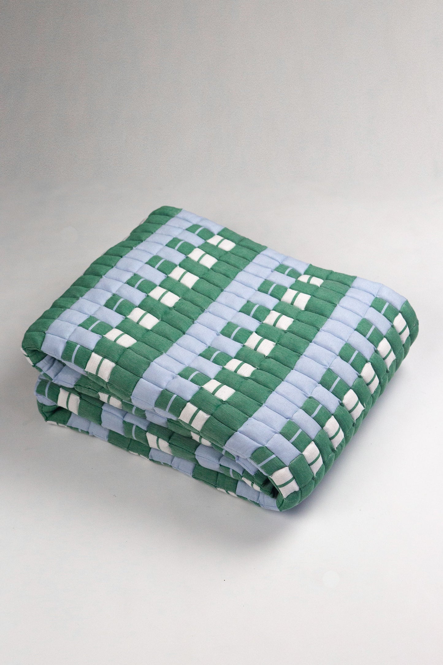 Folded quilt with green and blue checkered pattern on a light gray background