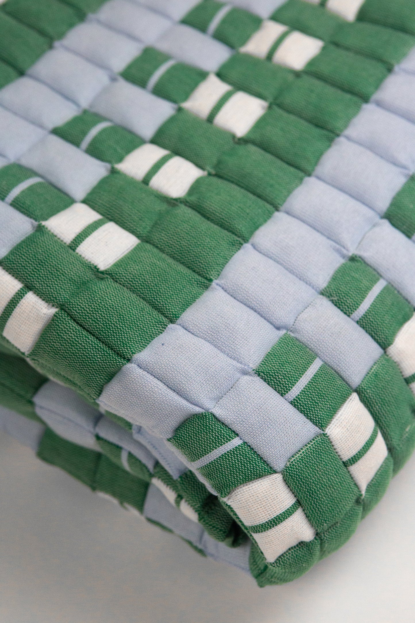 Stack of woven green and blue mats on a light background