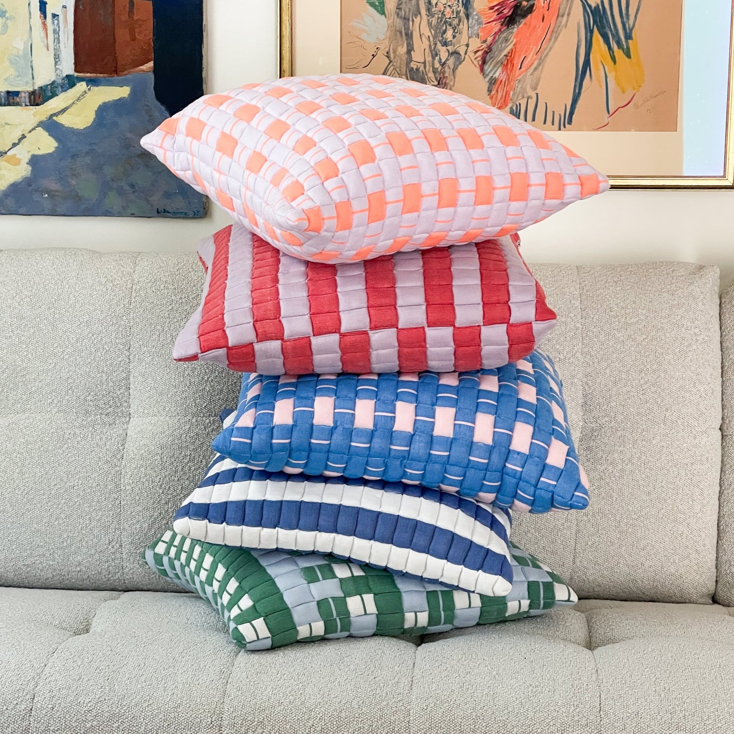 Stack of colorful checkered pillows on a gray sofa with abstract art in the background