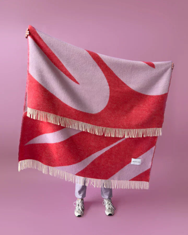 Red and white patterned blanket with fringes on a pink background