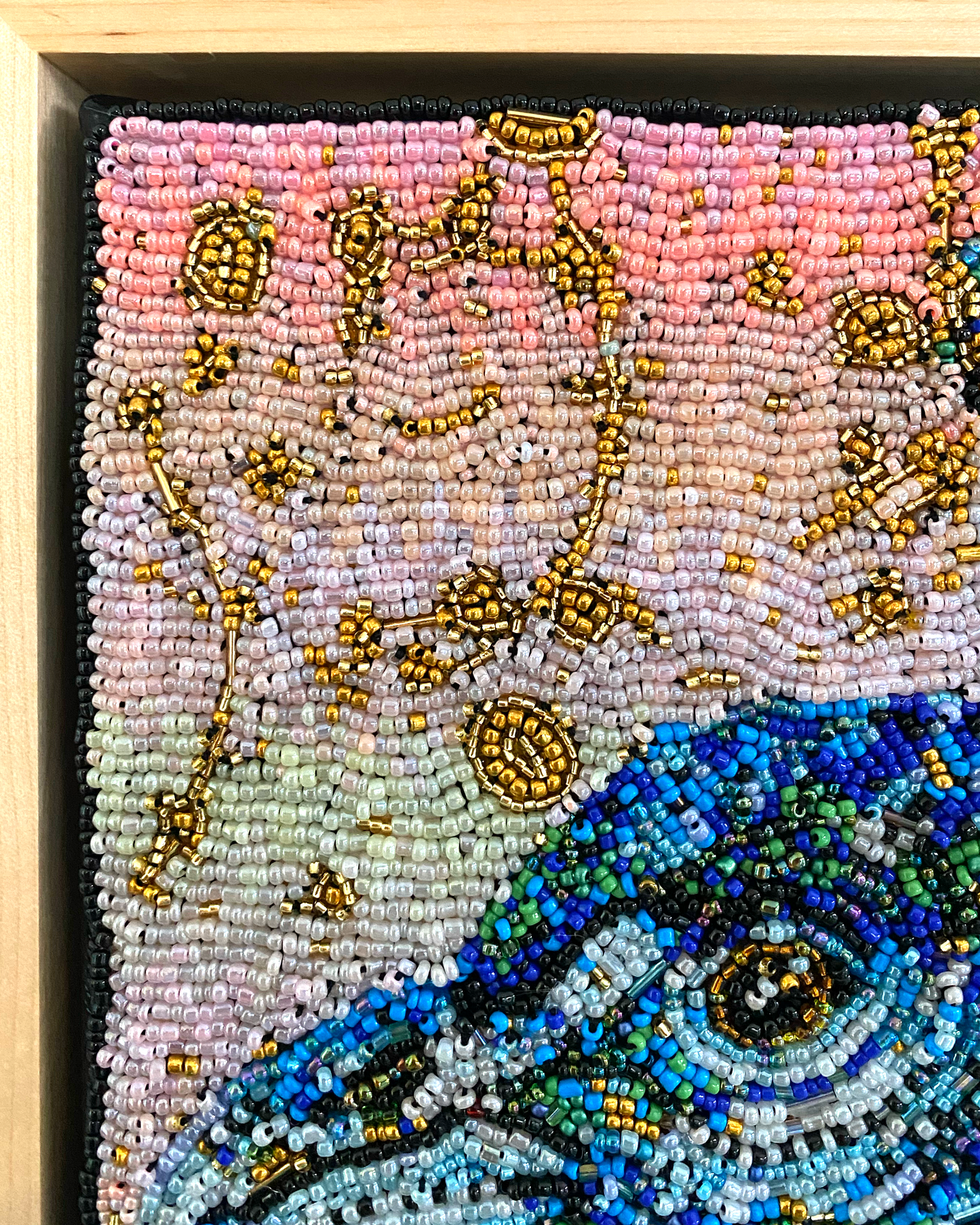 Close-up of a beaded artwork with a colorful bird design on a pink background.