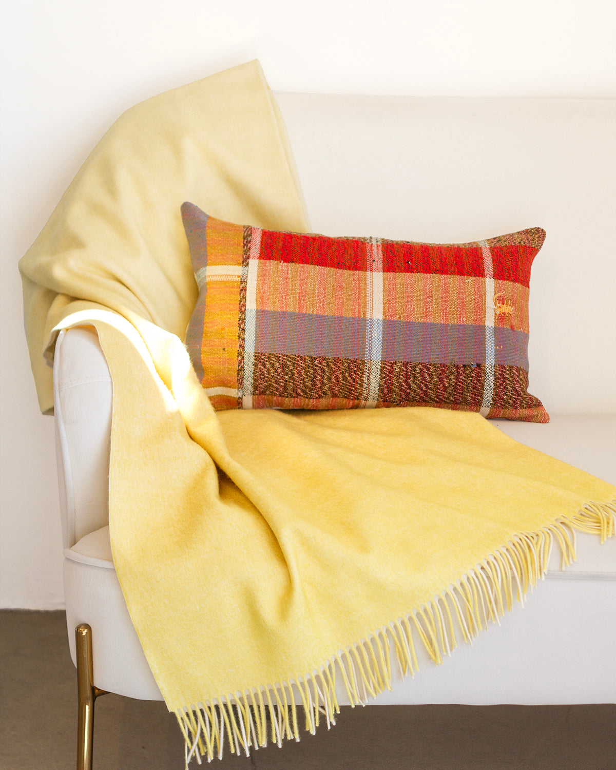 Yellow blanket draped over a white chair with a plaid pillow on a neutral background