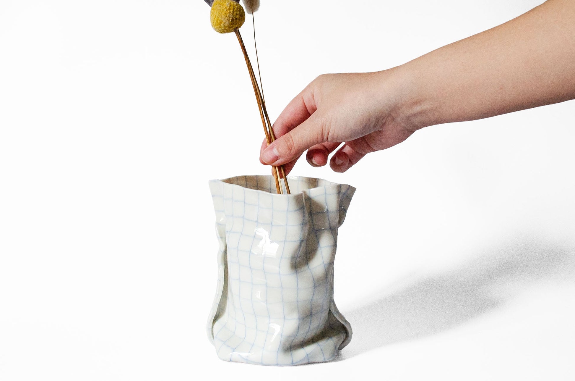 Hand placing a dried flower into a marble-patterned vase on a white background