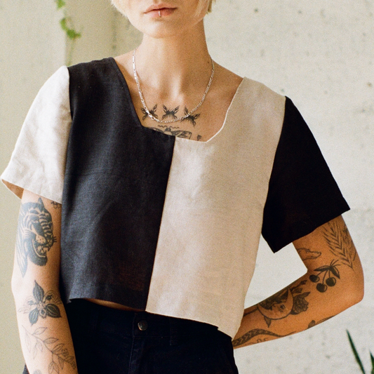 Person wearing a black and beige geometric top with tattoos on arms and neck.