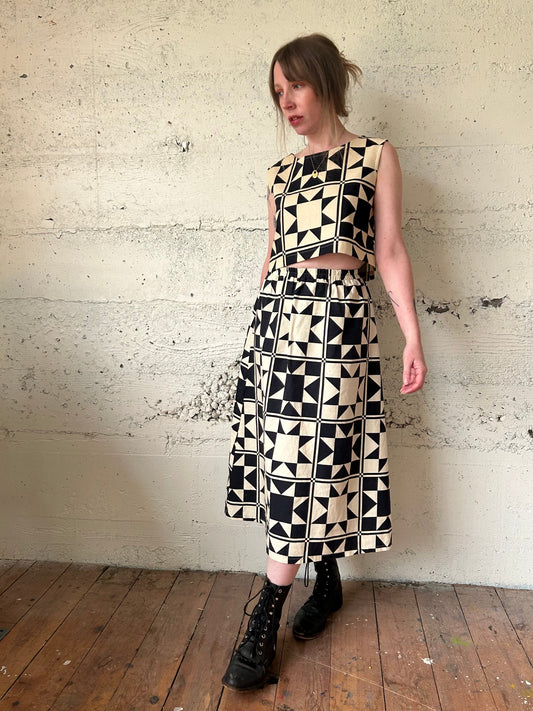 Woman wearing a black and white geometric patterned dress against a textured wall.
