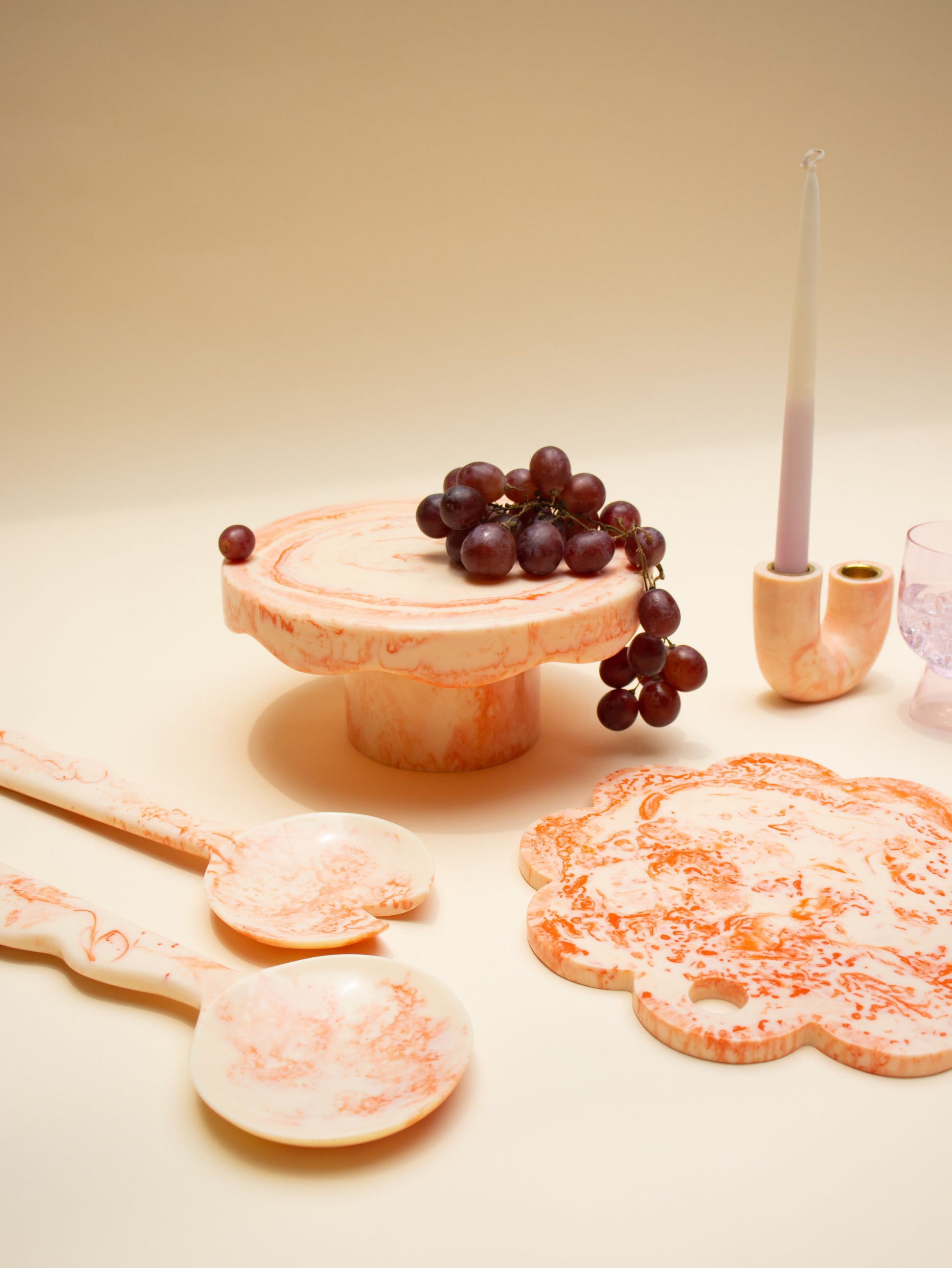 Decorative items including a wooden stand with grapes, cookies, and a candle on a beige surface.