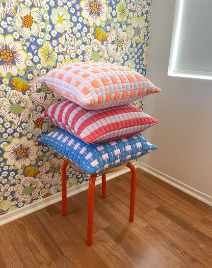 Stack of colorful checkered pillows on a stool against a floral wallpapered wall.