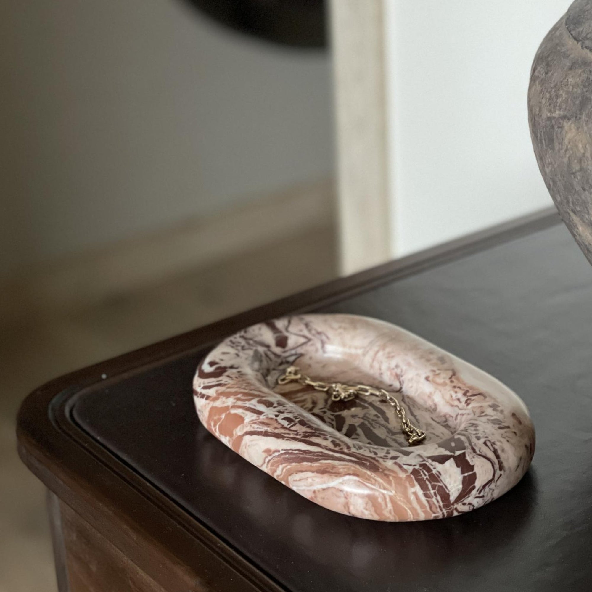 Marble-patterned jewelry dish with a gold chain on a wooden surface